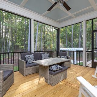 A cozy screened porch with wicker furniture overlooks a lush forest backdrop.