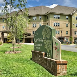 A view of a residential building with a decorative sign in front, surrounded by greenery.