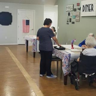 A caregiver interacts with residents in a dining area of a care facility.