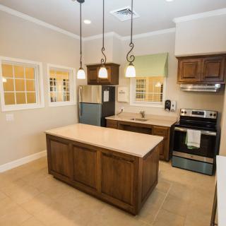 A modern kitchen featuring a central island, wooden cabinets, and overhead pendant lights.