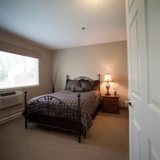 A cozy bedroom featuring a bed with a metal frame, a nightstand with a lamp, and a large window letting in natural light.