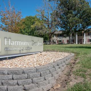 A landscaped area in front of a building, featuring a sign with trees and a clear blue sky.