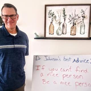A man stands next to a sign with inspirational advice in a home setting.