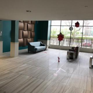 A spacious and modern lobby area with a sofa, table, and decorative elements, illuminated by natural light from large windows.