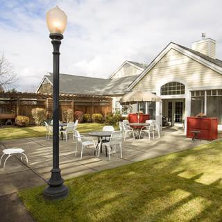 A cozy outdoor patio area with tables and chairs next to a building, featuring a lamp post and neatly maintained garden.