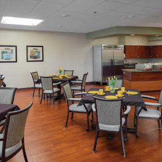 A spacious dining area featuring neatly arranged tables and chairs, with a modern kitchen in the background.