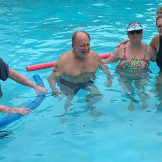 A group of people enjoying a swim in the pool with pool noodles.