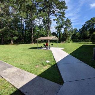 A peaceful park scene with a pavilion, surrounded by trees and grass under a clear blue sky.