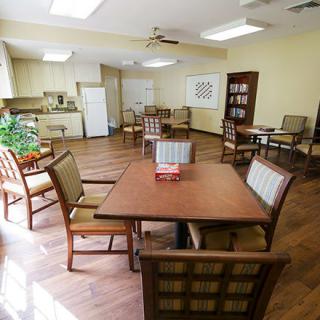 A spacious and well-lit room with a dining area featuring tables and chairs, adjacent to a small kitchen.