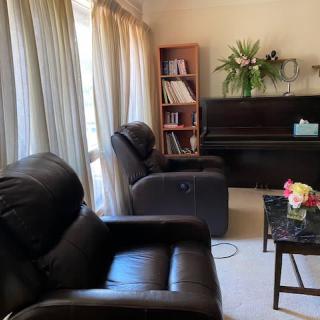 A cozy living room with a piano, armchairs, a bookshelf, and a coffee table adorned with flowers.