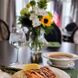 A beautifully arranged meal featuring grilled salmon with asparagus, rice, and a bowl of soup on a dining table adorned with a floral centerpiece.