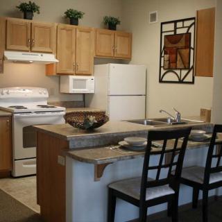 A modern kitchen with wooden cabinets, a white refrigerator, stove, and microwave. A countertop with bar stools creates a cozy dining area.