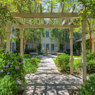 A serene garden pathway under a wooden pergola leading to a charming house.