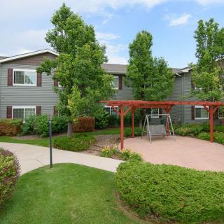 A well-maintained apartment complex with landscaped greenery, featuring a pergola and swing set on a paved pathway.