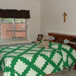 A cozy bedroom with a green and white quilt, a stuffed animal on the bed, and a cross hanging on the wall.