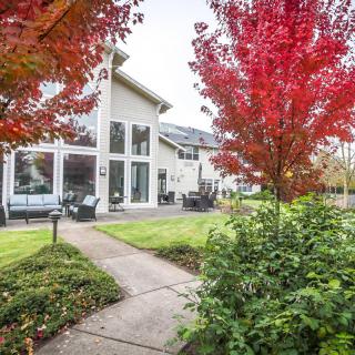 A modern house surrounded by a well-maintained yard with autumn trees displaying vibrant red foliage.