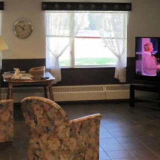 A cozy living room with floral chairs facing a television, with natural light coming through the window.