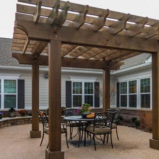 A cozy backyard patio with a wooden pergola providing shade over a set of outdoor furniture.