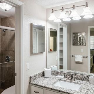 A modern bathroom with a granite countertop, sink, and well-lit mirrors.