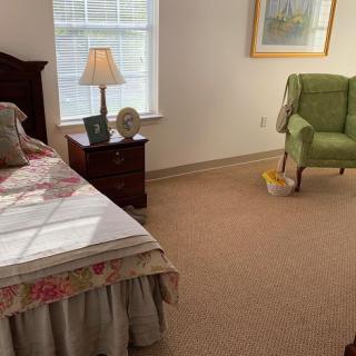 A cozy bedroom featuring a large bed, a wooden nightstand with a lamp, and a green armchair by the window.