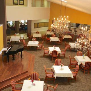 A spacious dining area featuring elegantly set tables, a grand chandelier, and a black piano.