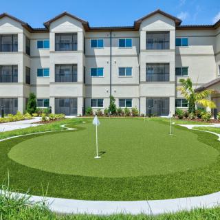 A modern apartment complex with a well-maintained putting green in the foreground.