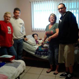 A group of people gathered in a bedroom, surrounding someone resting on a bed.