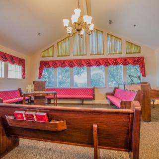 A serene church interior with red cushioned pews and a chandelier.