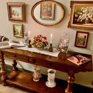 A cozy vintage-inspired console table adorned with framed art, candles, and decorative flowers.