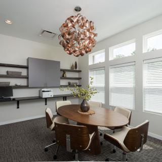 A modern conference room with a round table, comfortable chairs, and a stylish chandelier, flooded with natural light.