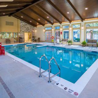 A modern indoor swimming pool with large windows and exposed wooden ceiling beams.