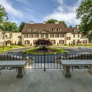 A grand mansion surrounded by lush gardens and featuring an elegant central fountain.