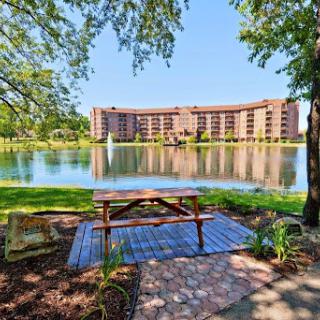 A serene view of a lake with a picnic table in the foreground and a building reflecting on the water.
