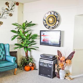 A cozy living room corner featuring a teal armchair, a large potted plant, a guitar amplifier, and fall-themed decorations.