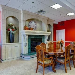 A dining room with a wooden table and chairs, featuring a decorative fireplace and red accent wall.