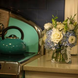 A vintage kitchen setting with a teal teapot and a bouquet of blue and white flowers.