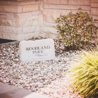 A stone sign reading 'Woodland Park' surrounded by small plants and gravel.