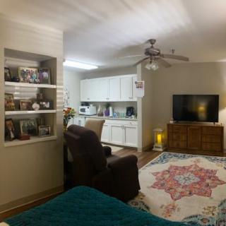 A cozy living room with an open kitchenette, featuring a large rug, armchair, and television.