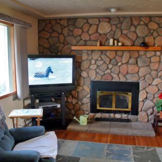 A cozy living room featuring a stone fireplace, a television, and a comfortable chair.