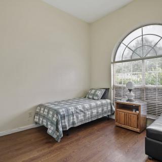 A cozy bedroom with a single bed, nightstand, and large window allowing natural light to fill the space.