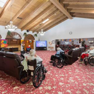 A cozy communal living room in a nursing home, featuring residents in wheelchairs watching television.