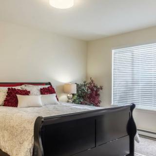 A cozy bedroom with a dark wooden bed frame, adorned with red and white pillows, next to a large window with blinds.