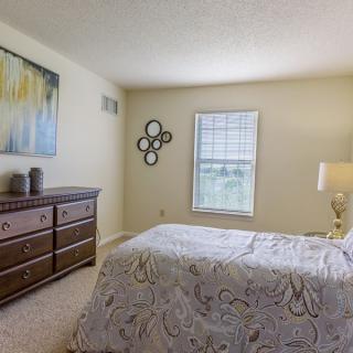 A cozy bedroom featuring a bed, dresser, window, and decorative artwork on the wall.
