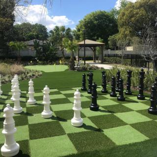 A large outdoor chess set in a garden with a gazebo and surrounding trees.