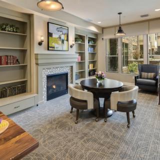 A cozy living room with a fireplace, surrounded by bookshelves and a central table with chairs.