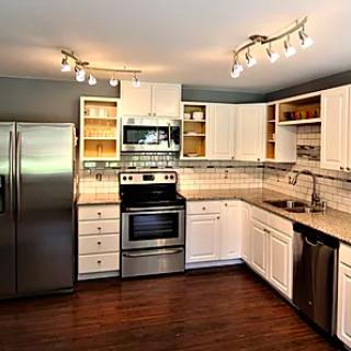 A modern kitchen with stainless steel appliances and white cabinetry, featuring hardwood floors and track lighting.