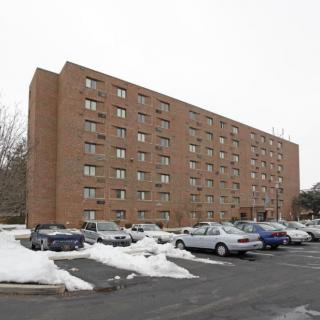 A multi-story brick apartment building with a snow-covered parking lot and several parked cars.