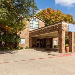 A brick hotel entrance with a covered driveway surrounded by trees.