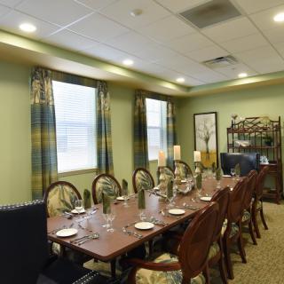 An elegantly set dining room with a long table, chairs, and decorative candles near curtained windows.