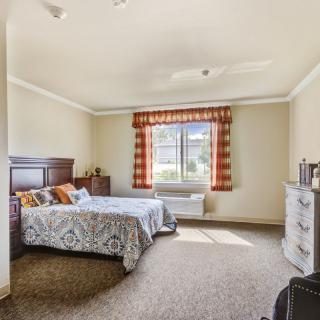 A cozy bedroom with a bed, dresser, and a window letting in natural light.